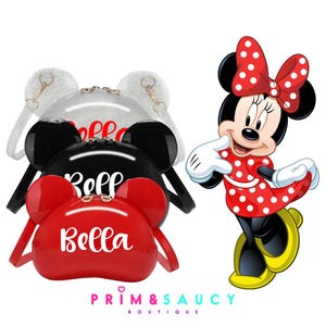 Puede incluir: Bolsos de Minnie Mouse de color rojo, negro y plateado con orejas negras y el nombre "Bella" escrito en blanco en el bolso rojo.