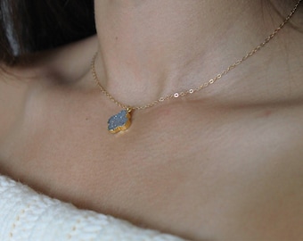 May include: A delicate gold chain necklace with a light blue, crystal-like pendant. The pendant is shaped like a four-leaf clover.