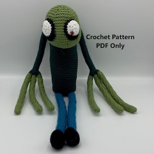 May include: Green crocheted amigurumi toy with large white eyes and red pupils. The toy has long green arms and blue legs with black feet. The toy is sitting on a white surface. Crochet Pattern PDF Only.