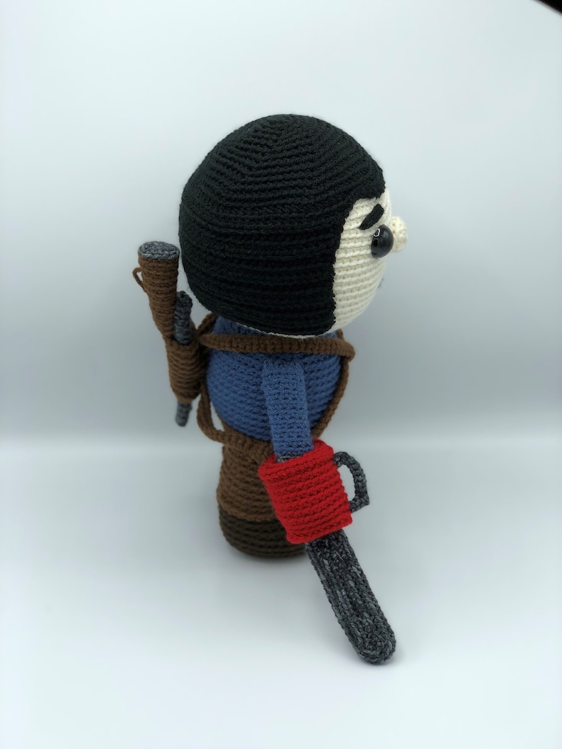 K&ouml;nnte beinhalten: Geh&auml;kelte Puppe eines Charakters mit schwarzer M&uuml;tze, blauem Hemd und braunem Geschirr. Die Puppe hat einen Kettens&auml;genarm mit rotem Griff und eine Schrotflinte. Einzigartiges Design, handgefertigt.