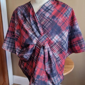 Könnte beinhalten: Ein roter, schwarzer und weißer karierter Stoffscarf mit einem geknoteten Design. Der Schal ist über eine weiße Schaufensterpuppe gelegt.