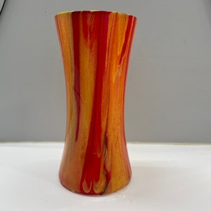 May include: A decorative vase with a flared top and base, featuring a vibrant blend of red, orange, and yellow hues. The colors are swirled and streaked, creating a unique, artistic pattern. The vase is approximately 8 inches tall.