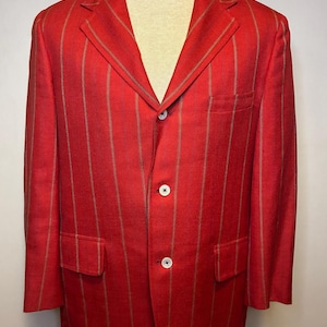 May include: A bright red blazer featuring vertical tan pinstripes, a notched lapel, and a three-button front closure. The jacket includes two lower flap pockets and a single chest pocket, displayed on a neutral-colored mannequin torso.