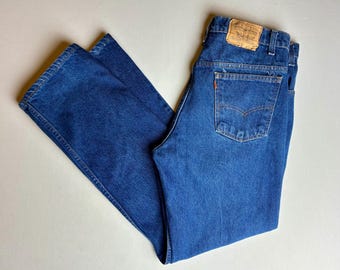 Könnte beinhalten: Blaue Jeans aus Denim mit klassischem Fünf-Taschen-Design. Die Jeans haben einen geraden Bein-Schnitt und ein orangefarbenes Levi's-Etikett auf der Gesäßtasche. Die Jeans liegen flach, wodurch die Details der Nähte und des Denim-Stoffs hervorgehoben werden.