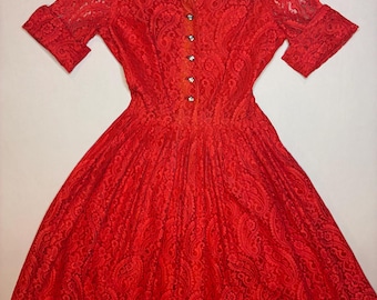Könnte beinhalten: Ein leuchtend rotes Spitzenkleid mit kurzen Ärmeln und einem Kragen. Das Kleid hat eine Knopfleiste vorne und eine taillierte Taille mit einem ausgestellten Rock. Das aufwendige Spitzenmuster verleiht dem Kleid Textur und Details.