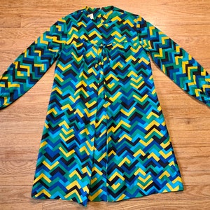 May include: A blue, green, yellow, and black patterned dress with long sleeves and a tie at the neck.