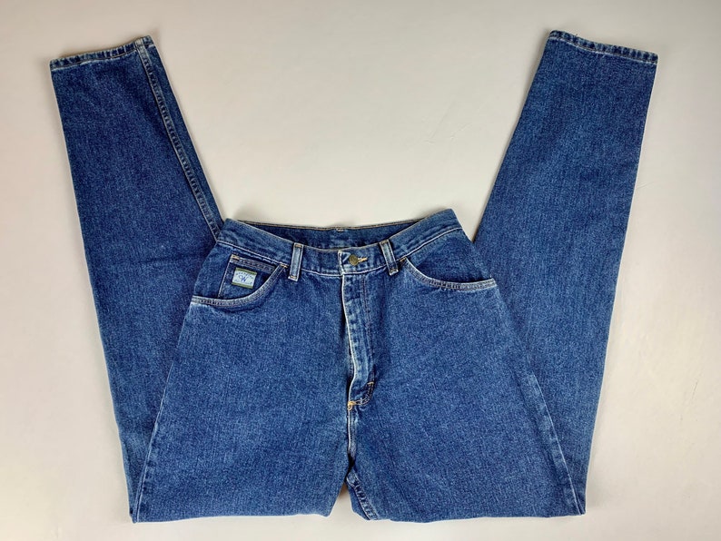 May include: A pair of high-waisted blue denim jeans with a light blue patch on the right pocket that says "Wrangler".
