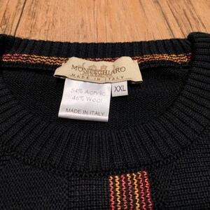 Peut inclure: Pull-over noir &agrave; rayures orange, jaune et rouge. L'&eacute;tiquette indique "Montechiaro Made in Italy" et "54% Acrylique 46% Laine" avec une &eacute;tiquette de taille indiquant "XXL".