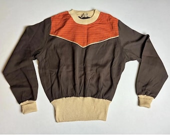 Könnte beinhalten: Ein Vintage-Pullover in Braun, Orange und Beige. Das obere Joch ist orange mit einem Gittermuster, das mit Beige umrandet ist. Der Körper ist braun, mit beigefarbenen Rippbündchen, Kragen und Bund. Ein Retro-Modestück.