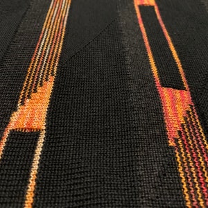Peut inclure: Gros plan sur un tissu noir tricot&eacute; avec des rayures verticales orange, rouge et blanches.