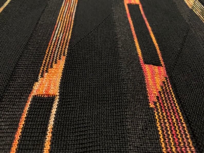 Peut inclure: Gros plan sur un tissu noir tricot&eacute; avec des rayures verticales orange, rouge et blanches.