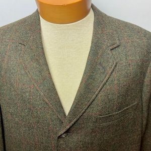 May include: A green tweed blazer with a red plaid pattern. The blazer has a notched lapel, a single-button closure, and a chest pocket. The jacket is made of a textured fabric.