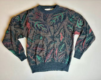 Könnte beinhalten: Ein langärmliger Pullover mit einem Blattmuster in Grau-, Türkis- und Rosatönen. Der Pullover hat einen gerippten türkisfarbenen Kragen, Bündchen und Saum. Das Blattmuster ist über Körper und Ärmel verteilt.