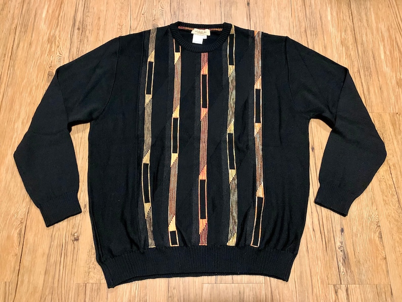 Peut inclure: Pullover noir &agrave; manches longues avec un motif g&eacute;om&eacute;trique en marron, or et orange.