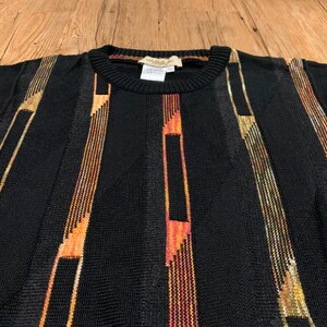 Peut inclure: Pullover noir &agrave; rayures verticales dans des tons d'orange, d'or et de brun.