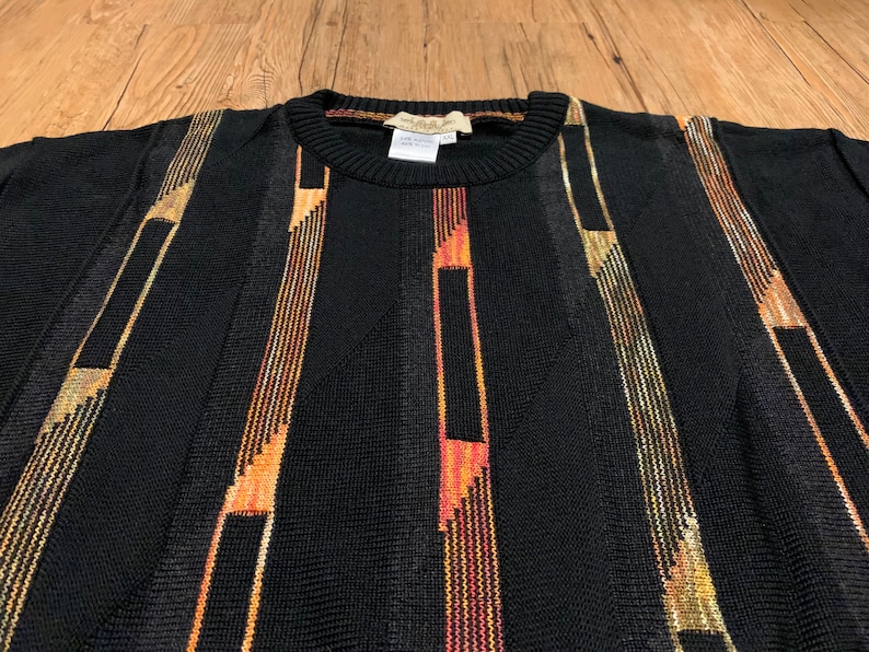 Peut inclure: Pullover noir &agrave; rayures verticales dans des tons d'orange, d'or et de brun.