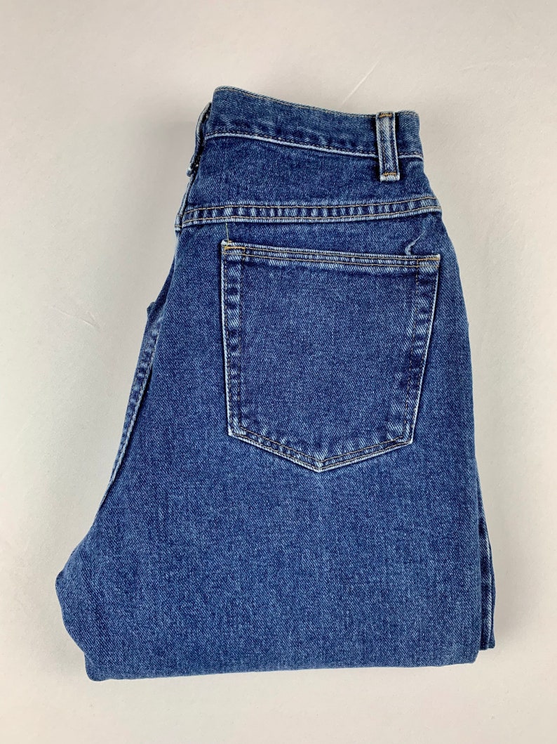 May include: A pair of blue denim jeans folded in half. The jeans have a back pocket and a button fly.