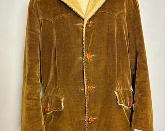 Könnte beinhalten: Braune Cordjacke mit beigem Kunstfellkragen und -futter. Die Jacke hat vier braune Knöpfe vorne, zwei Vordertaschen und ein beiges Futter, das an den Manschetten und Taschen sichtbar ist.