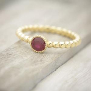 May include: A gold ring with a red ruby gemstone set in a beaded band.