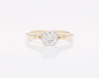 May include: A gold ring with a single round diamond set in a prong setting. The diamond is surrounded by smaller diamonds.