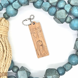 May include: Wooden keychain with a silver chain. The keychain has a rectangular wooden tag with the words "Come Follow Me" and a line drawing of Jesus Christ.