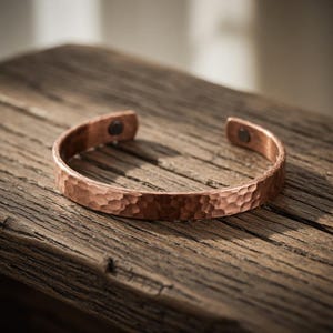 Peut inclure: Un bracelet manchette en cuivre avec une texture martelée. Le bracelet ouvert est doté d'une fermeture magnétique. Le bracelet est présenté sur une surface en bois vieilli. La couleur cuivre est un brun-rouge chaud.