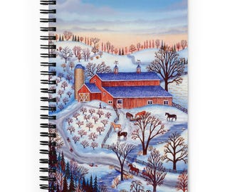 May include: Spiral-bound notebook featuring a winter landscape painting. The artwork depicts a red barn with a blue roof, a silo, and several horses in a snowy field. Bare trees and a winding road lead to the barn under a blue sky.