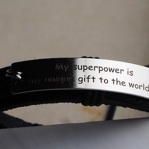 May include: Black leather bracelet with a silver metal tag that reads "My superpower is my unique gift to the world."