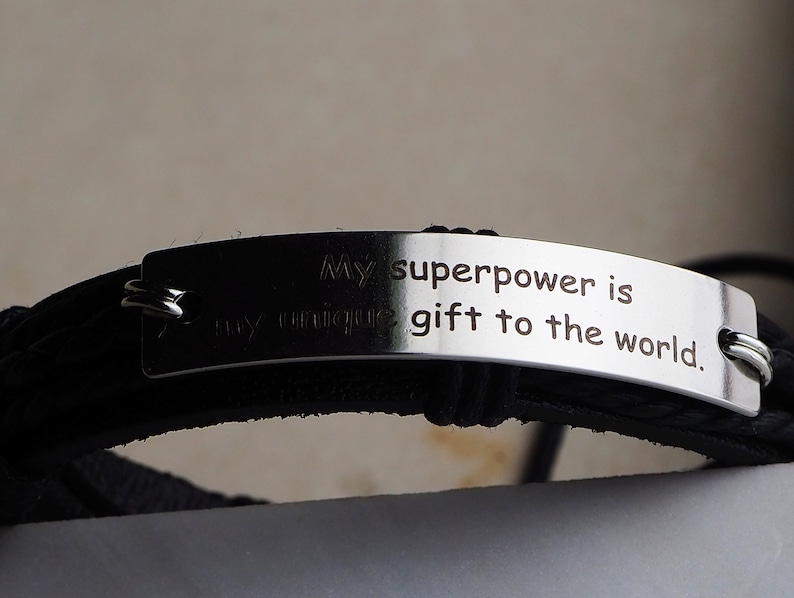 May include: Black leather bracelet with a silver metal tag that reads "My superpower is my unique gift to the world."