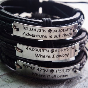 May include: Three black leather bracelets with silver metal tags. The tags have coordinates and phrases engraved on them: "35.33433°N 94.30138°W Adventure is out there", "44.00015°N 84.40453°W Where I belong", and "50°42'47"N 1°59'25"W Where it all began".