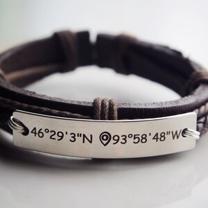 May include: A brown leather bracelet with a silver plate engraved with the coordinates "46°29' 3"N 93°58' 48"W".