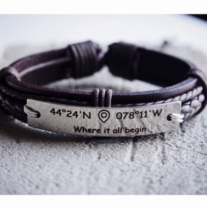 May include: A brown leather bracelet with a silver plate engraved with the coordinates "44&deg;24'N 078&deg;11'W" and the text "Where it all begin".