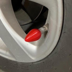 May include: A close-up of a red valve stem cap on a car tire.