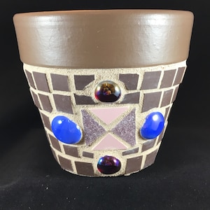 Puede incluir: Una maceta de terracota marrón con un diseño de mosaico. El mosaico está hecho de pequeñas baldosas marrones y presenta detalles en vidrio rosa, azul y morado.