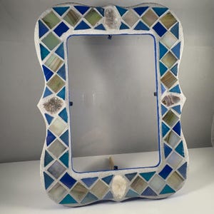 May include: A decorative rectangular picture frame with a mosaic design. The frame features a mix of blue, teal, and white tiles arranged in a diamond pattern. The frame's edges are a light gray color, and it has decorative stone accents.