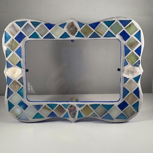 May include: A rectangular mirror with a mosaic tile frame. The frame features a mix of blue, white, and green diamond-shaped tiles, with shell accents. The mirror has a decorative, scalloped edge and a silver-colored border.