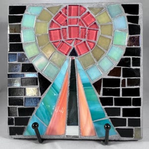 Pode incluir: Um azulejo de mosaico colorido com um design geométrico. O azulejo apresenta um círculo vermelho no centro, rodeado por um anel de azulejos amarelos, verdes e azuis. O azulejo está colocado sobre um fundo preto.