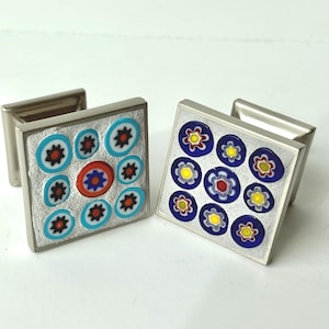 May include: A pair of square cufflinks with a silver-coloured metal frame. Each cufflink has a mosaic design with colourful floral patterns in red, blue, yellow, and white. The cufflinks have a rectangular post.