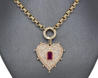 May include: Gold-toned necklace with a heart-shaped pendant. The pendant is encrusted with small, clear stones and features a rectangular, ruby-colored stone in the center. The necklace is displayed on a black mannequin.