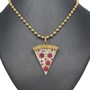 May include: A gold chain necklace with a pizza slice pendant. The pendant is covered in small diamonds and red rubies.