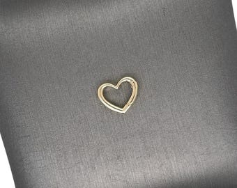 May include: A gold-colored heart-shaped clasp is centered on a dark gray, square pillow. The clasp is a simple, elegant design. The pillow has a textured surface.
