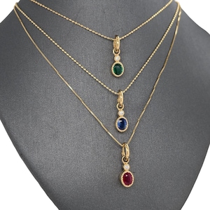 May include: Three gold necklaces with different colored gemstones. The top necklace has a green gemstone, the middle necklace has a blue gemstone, and the bottom necklace has a red gemstone. Each gemstone is surrounded by a small circle of diamonds.