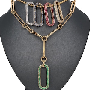 Puede incluir: Un collar de cadena de oro con cinco colgantes. Cada colgante tiene forma rectangular con una piedra preciosa de color diferente engastada en el centro. Las piedras preciosas son azules, rojas, blancas y verdes.