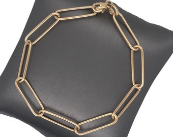 Peut inclure: Un bracelet à maillons de couleur or avec un design ovale allongé. Le bracelet est présenté sur une surface gris foncé. Le fermoir est visible et les maillons sont espacés de manière uniforme, créant un look moderne et élégant.