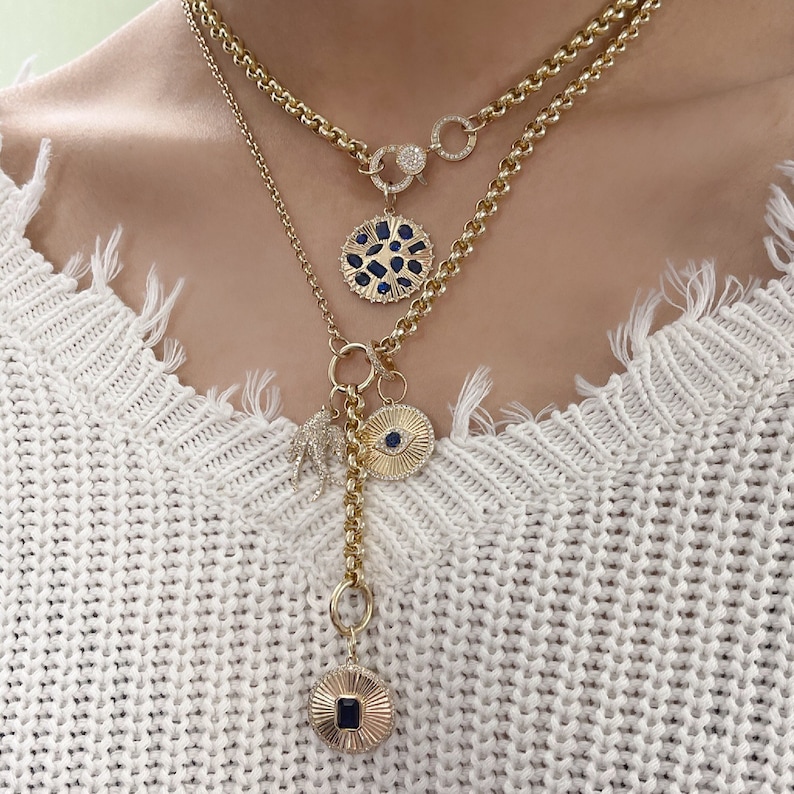 May include: A gold layered necklace with multiple charms, including a blue eye charm, a blue and gold circle charm, and a gold bird charm.