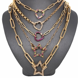 Puede incluir: Cinco collares de oro con diferentes colgantes de corazón y estrella de piedras preciosas de colores. Los collares están superpuestos en un busto de maniquí gris.