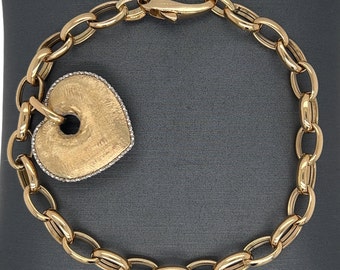 Op de afbeelding: Een gouden kettingarmband met een grote hartvormige hanger. De hartvormige hanger heeft een getextureerd oppervlak en is versierd met kleine diamanten rond de rand.