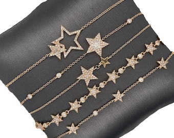 May include: Five gold bracelets with diamond star charms. The bracelets feature different styles of stars, including a large open star, a smaller filled-in star, and a smaller star with a single diamond in the center. The bracelets are arranged on a gray velvet surface.