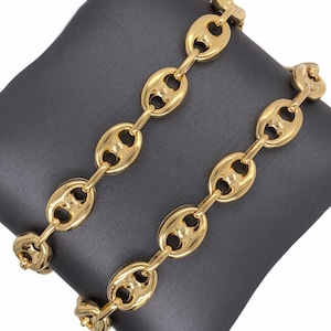 K&ouml;nnte beinhalten: Zwei goldfarbene Kettenarmb&auml;nder mit einem markanten, aufgebl&auml;hten ovalen Gliederdesign. Die Glieder sind durch kleinere, l&auml;ngliche Glieder verbunden. Die Armb&auml;nder werden auf einer dunkelgrauen Oberfl&auml;che pr&auml;sentiert, die ihre gl&auml;nzende, reflektierende Oberfl&auml;che hervorhebt.