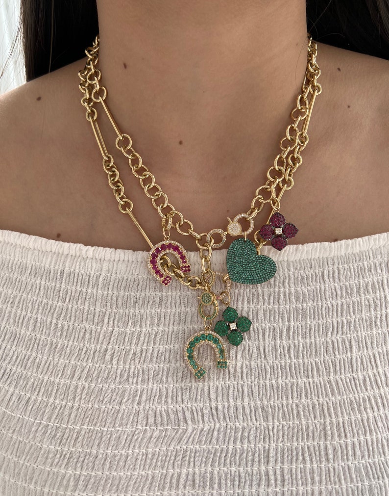 May include: A gold chain necklace with multiple charms. The charms are a green heart, a green four-leaf clover, a red horseshoe, and a red flower. The charms are all covered in sparkling stones.